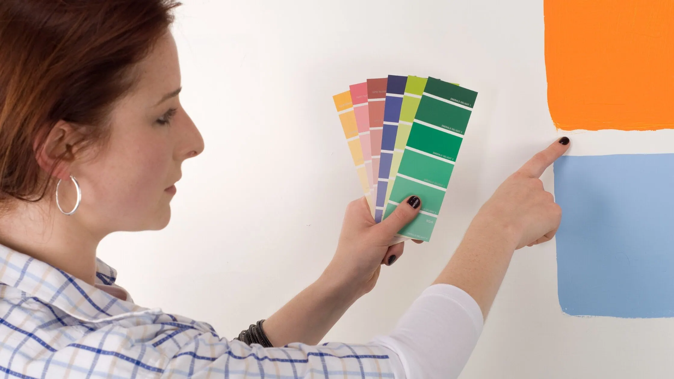 Woman selecting paint colors for a room, comparing swatches against vibrant wall samples.