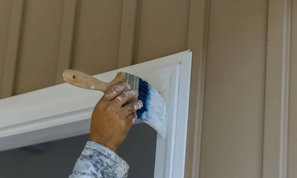 Close-up of a hand painting white door trim for a home improvement project.